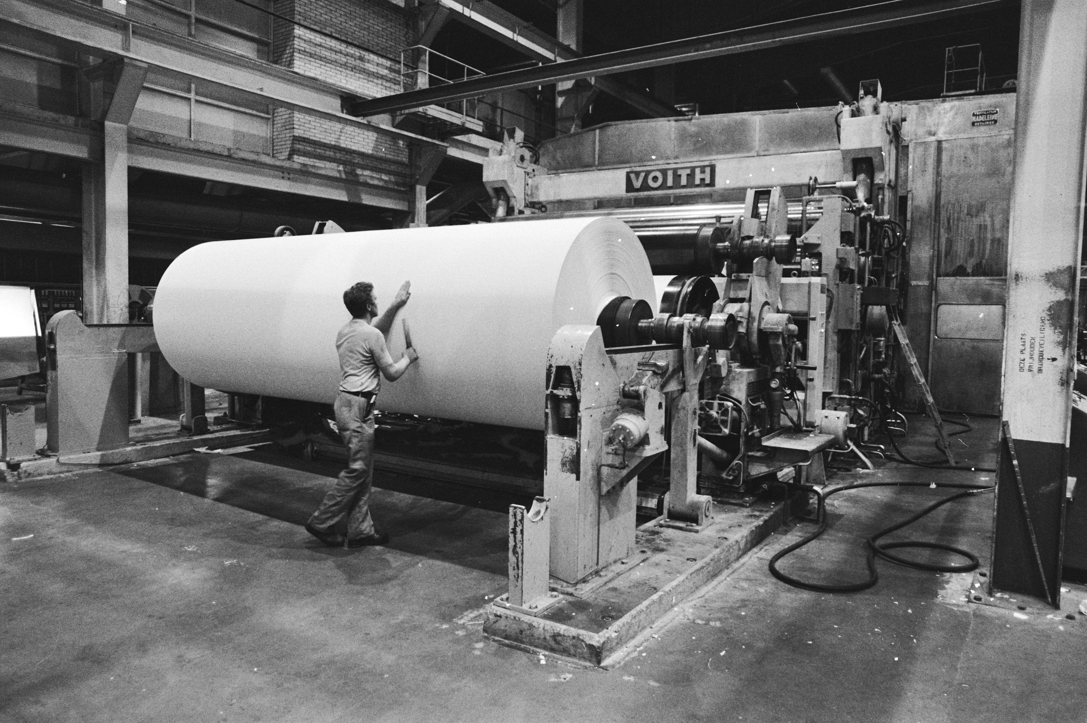 Operarios junto a grandes bobinas de papel en una nave industrial